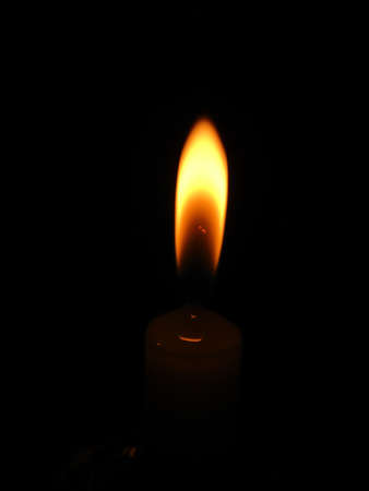 In the dark night there is a candle lit with a bright and colorful flame.の写真素材