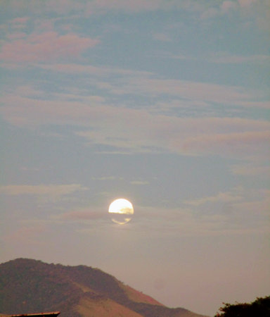 Illuminated full moon setting against a backdrop of mountain and sky with few clouds.の写真素材