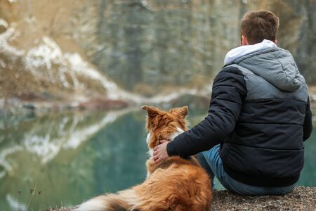 Young man sitting near to clear lake with his dogの写真素材