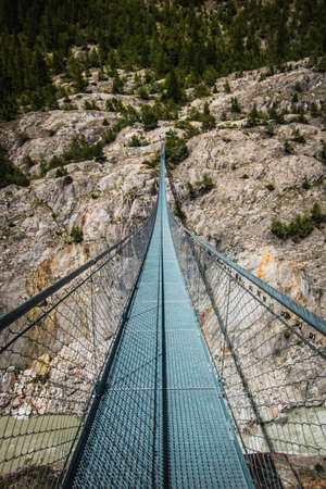 Wooden long footbridge above the deep gorge with a river at the bottom, between the rocks. Wild mountains in Swiss Alps - bridge in Switzerlandの写真素材