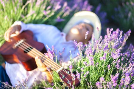 A country boy lies in a lavender field and plays the ukulele. The main subject is out of focus.の写真素材