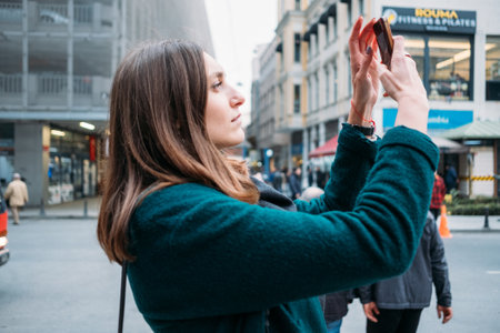 TURKEY, ISTANBUL, DECEMBER 14, 2018: Beautiful girl in a coat takes pictures by smartphone on the Istiklal roadのeditorial素材