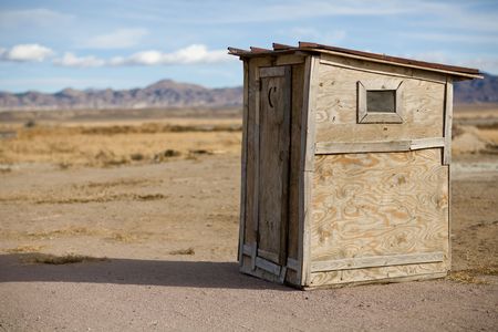 Old wooden outhouse on a remote highway in Nevada with mountains and blue sky with clouds in the background and scrub brush all around.  A moon and star are cut out of the door for light.の写真素材