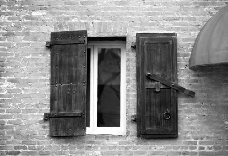 Window with wooden shutters in old brick building.  Image in black and white.