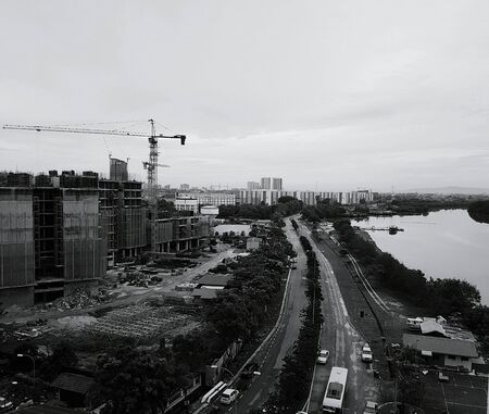 Black and white image of cityscape with construction site, road below by the river