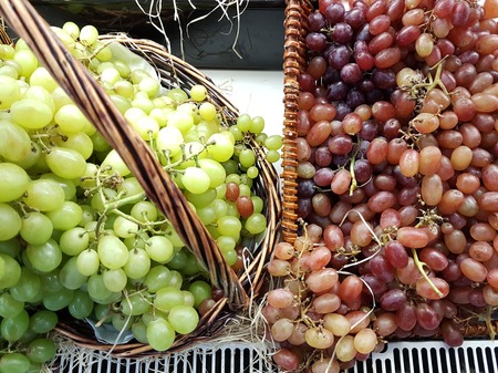 Close-up image comparison of two different colored grapes, green and purple side by side on sale in...