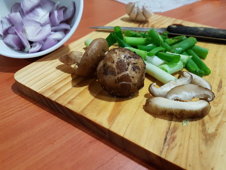 Close-up of Food preparation- mushroom, whole and sliced with spring onion, onions and garlic ingredients with knife for cooking on wooden cutting boardの写真素材