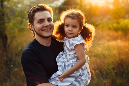 Family portrait of four in autumn forest park with little girls twins. Happy people, smiling and kissing. Warm evening sunlightの写真素材
