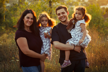 Family portrait of four in autumn forest park with little girls twins. Happy people, smiling and kissing. Warm evening sunlightの写真素材