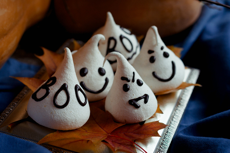 Funny meringue ghosts for Halloween party on autumn decorations. Golden leaves, pumpkin, blue textil and light of candles.の写真素材