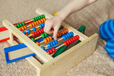 Hand of little boy playing with abacus. Clouse up picture of curly cute toddler playing with wooden toy.の写真素材