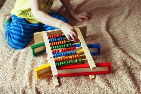 Hand of little boy playing with abacus. Clouse up picture of curly cute toddler playing with wooden toy.の写真素材