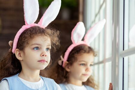 Cute little child girls twins wearing bunny ears on Easter day. Sister looking at windowの写真素材