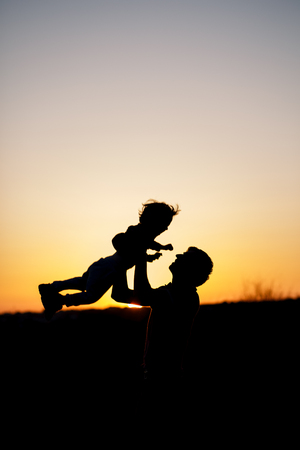 Silhouette of a man and his son playing together outdoor at sunset. Vertical photo. Family conceptの写真素材