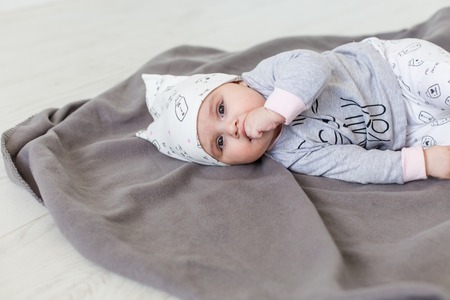 Cute baby lying on a grey blanket and keeps fingers in his mouth. Happy childhood concept. First...