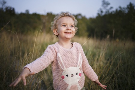 Cute curly hair blonde girl. Toddler in pink sweater. Outdoor baby portrait.