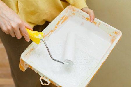 Photo of a female painting a wall with a roller and white paint. Horizontal photo. Copy spaceの写真素材