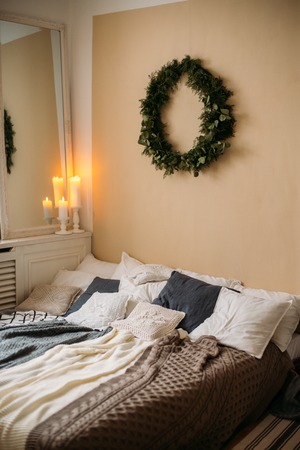 Bright cozy modern bedroom with holiday decoration. Bed with grey bedding set and knitted pillow on it, wooden rack, beautifulの写真素材
