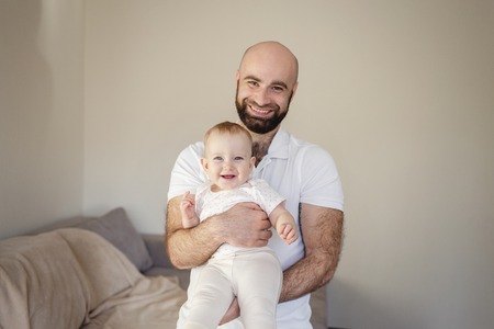 Portrait of masculine adult bearded man with strong body in perfect fit with baby on hands . Loving Father holding and taking care of adorable infant daugter. Cute smiling girlの写真素材