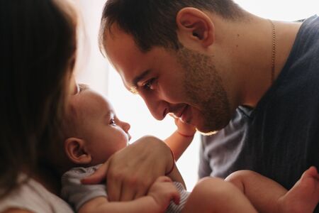Baby with his parents playing on the bed. Happy family at home. Lifestyle cozy photos. Little boy 4 months oldの写真素材