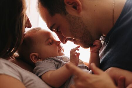 Baby with his parents playing on the bed. Happy family at home. Lifestyle cozy photos. Little boy 4 months oldの写真素材