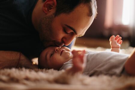 Attractive young father leaning in to kiss his baby boy. Fathers love concept