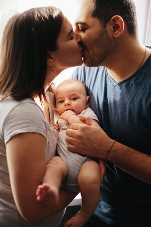 Young mother and father kissing each other with baby on hands. Close up portrait. Happy family...