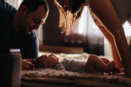 Baby with his parents playing on the bed. Happy family at home. Lifestyle cozy photos. Little boy 4 months oldの写真素材