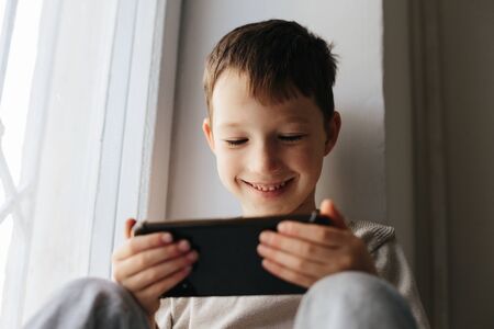 Little smiling child boy playing games or surfing internet on digital smartphone computer white isolatedの写真素材