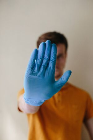 A man in medical rubber gloves raises his hand to signal to stay away and stay at a distance. Stop coronavirus. Focus on the hand. COVID-19 concept.の写真素材