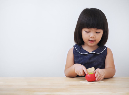 Funny asian kid girl playing with wooden cooking toy, Little chef preparing food on kitchen counterの写真素材