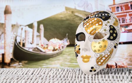 Mask from Venice with a gondola moored by Rialto Bridge. Golden and decorative souvenir and a traditional Venetian boat in the canal in the blurred background. Summer holiday and travel concept.の写真素材