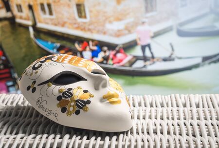 Authentic mask from Venice with a gondolier and tourists in gondola in the background. Golden souvenir and traditional Venetian boat in the world famous canal. Sunny summer travelling in Italy.の写真素材