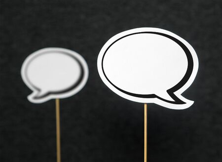 2 blank speech bubbles on a dark black background. The other speech balloon blurred. Chat bubble cut from paper with wooden stick. Discussion, protest and commenting concept with copy space for text.の写真素材