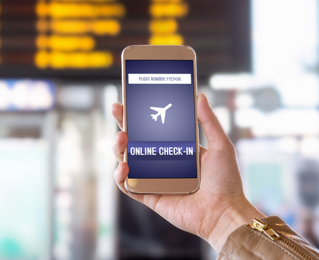 Online check in with mobile phone in airport. Woman checking in to flight with smartphone on the web. Internet self service provided by airline. Hand holding cellphone. Timetable in the background.の写真素材