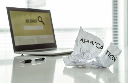 Out of work and frustration concept. Ripped job application paper on home office table with laptop...