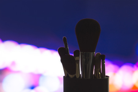 Make up brushes set silhouette with city lights. Outline of beauty products on blurred bokeh background. Cosmetics blenders in dark shadow at night lighting. Marketing for services or tutorials.の写真素材