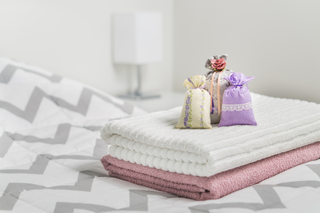 Scented sachets on towels on bed. Fragrant pouches for cozy home. Dried lavender in decoration bags in bedroom. Furnishing accessories and light color Scandinavian interior design. Aroma potpourri.の写真素材
