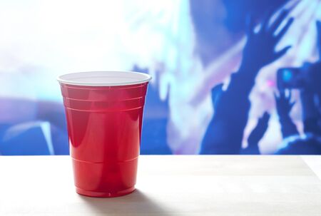 Plastic red party cup on a table. Nightclub full of people dancing on the dance floor in the...