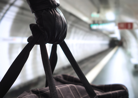 Close up of terrorist holding black bag in hand, possibly timebomb. Man planning a dangerous explosion in subway. Underground metro tunnel in the blurred background. Terrorism and security concept.の写真素材