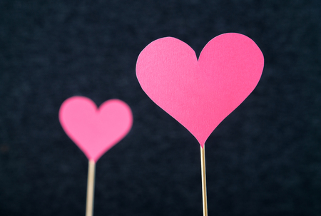 Two romantic hearts cut from cardboard or paper on wooden stick and dark background. Beautiful, handmade pink red love shapes. Simple anniversary, mother's, valentine's or women's day greeting card.の写真素材