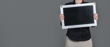 Woman holding chalkboard with copy space. Plenty of free blank room for text and content. Dark gray background. Girl with waitress or business style clothing showing empty blackboard.の写真素材