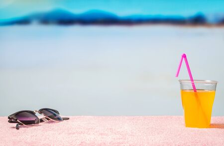 Vacation background with free blank copy space. Sunglasses and yellow cocktail with pink straw on beach. Beautiful lagoon beach paradise in blurred in the back. Perfect template for summer designs.の写真素材