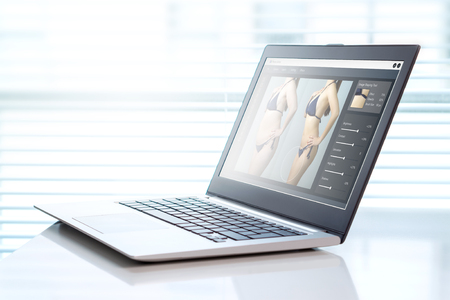 Image manipulation software in a laptop in office. Transforming girl skinnier and slim for marketing or advertisement. Photo editing and beauty standards concept.の写真素材