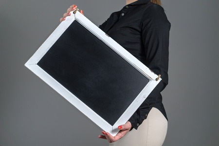 Woman holding tilted chalkboard on a dark gray background. Free blank empty copy space for text,...