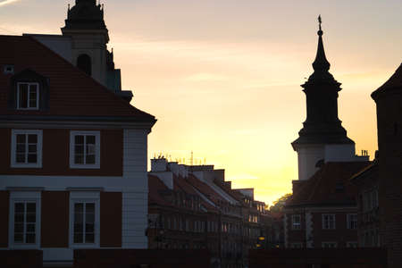 Sunset or sunrise in old town of Warsaw, Poland. Old buildings in dark shadow, almost silhouette. Beautiful yellow orange sky.の写真素材