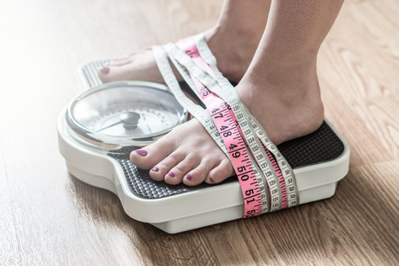 Anorexia and eating disorder concept. Feet tied up with measuring tape to a weight scale. Addiction and obsession to weight loss.の写真素材