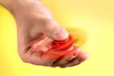 Red fidget spinner spinning fast between fingers against light yellow background.