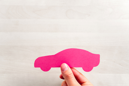 Car sale or loan, auto insurance, driving school or vehicle inspection and check up background or template with negative copy space. Buying new or used automobile. Hand holding a cardboard paper shapeの写真素材