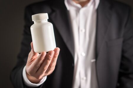 Pharmaceutical representative, consultant or head director or manager of medicine company with medicine bottle. Man in a suit holding pills or tablets in white container. Medical business concept.の写真素材